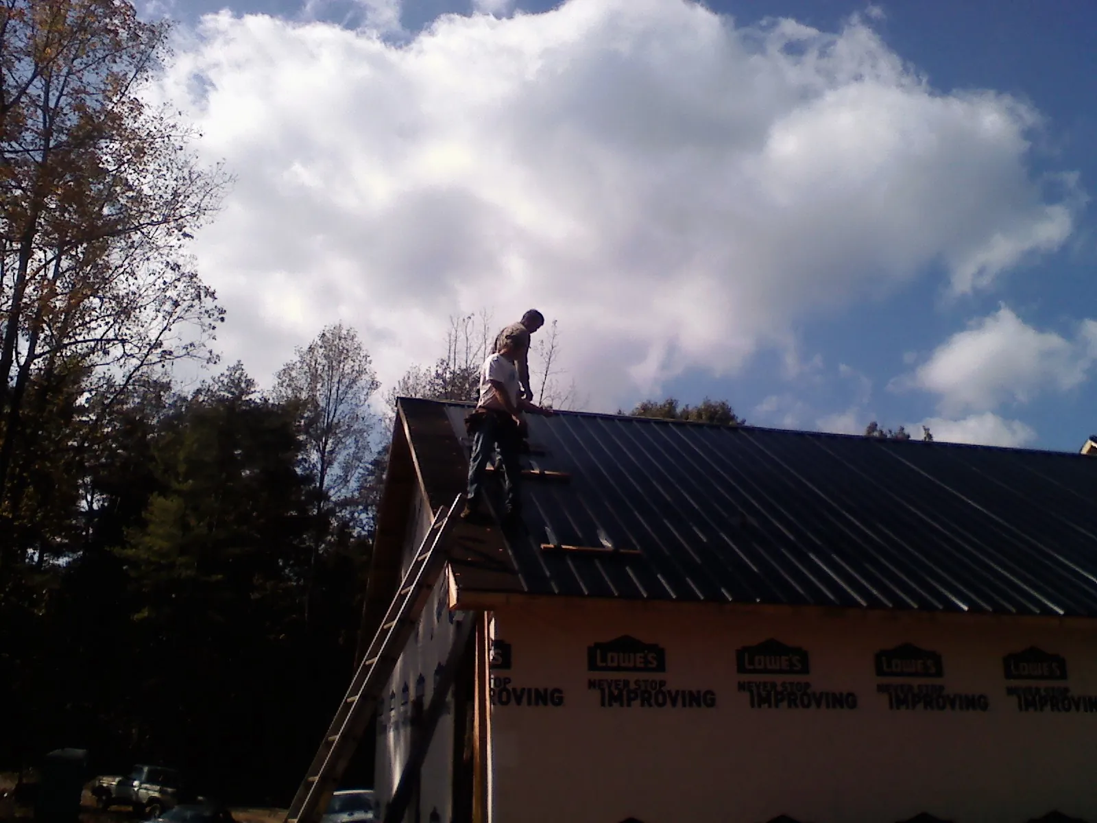 Roofer fastening dark metal panels high against a cloudy sky, from a Roof Inspection job in Surprise